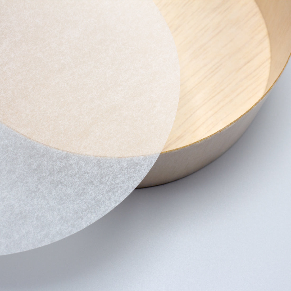 Washi feel translucent round piece of paper next to round wood container.